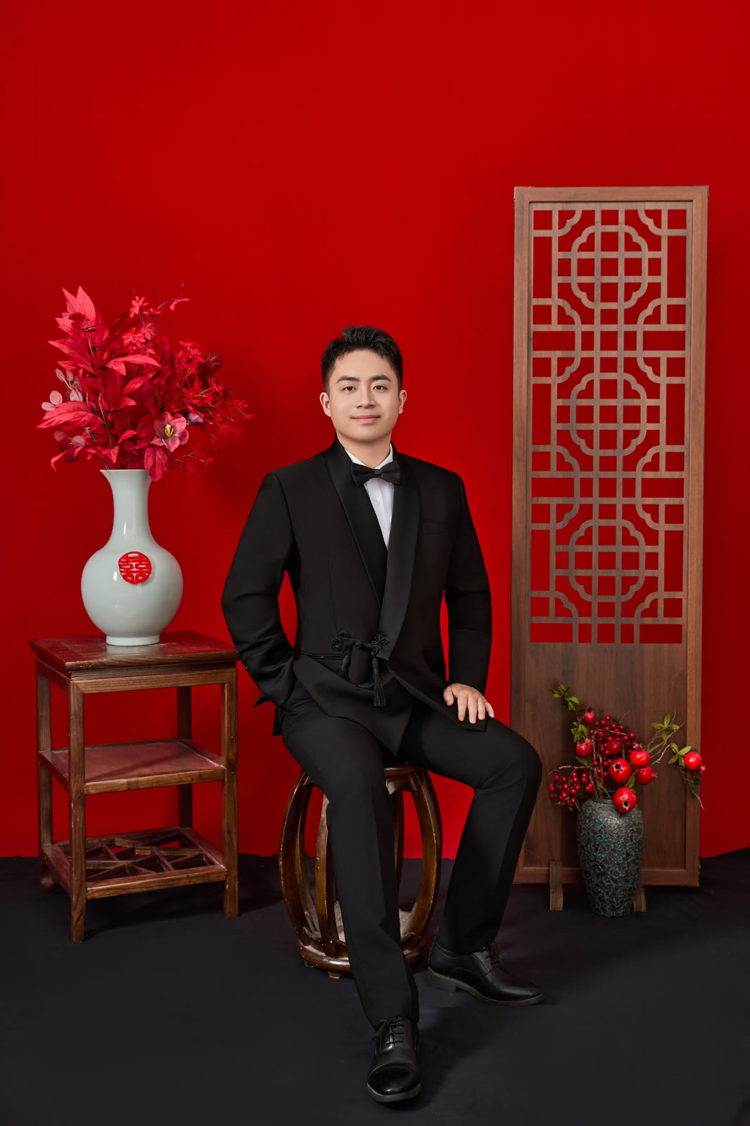 钱立勇身着黑色礼服，坐在红色布景前